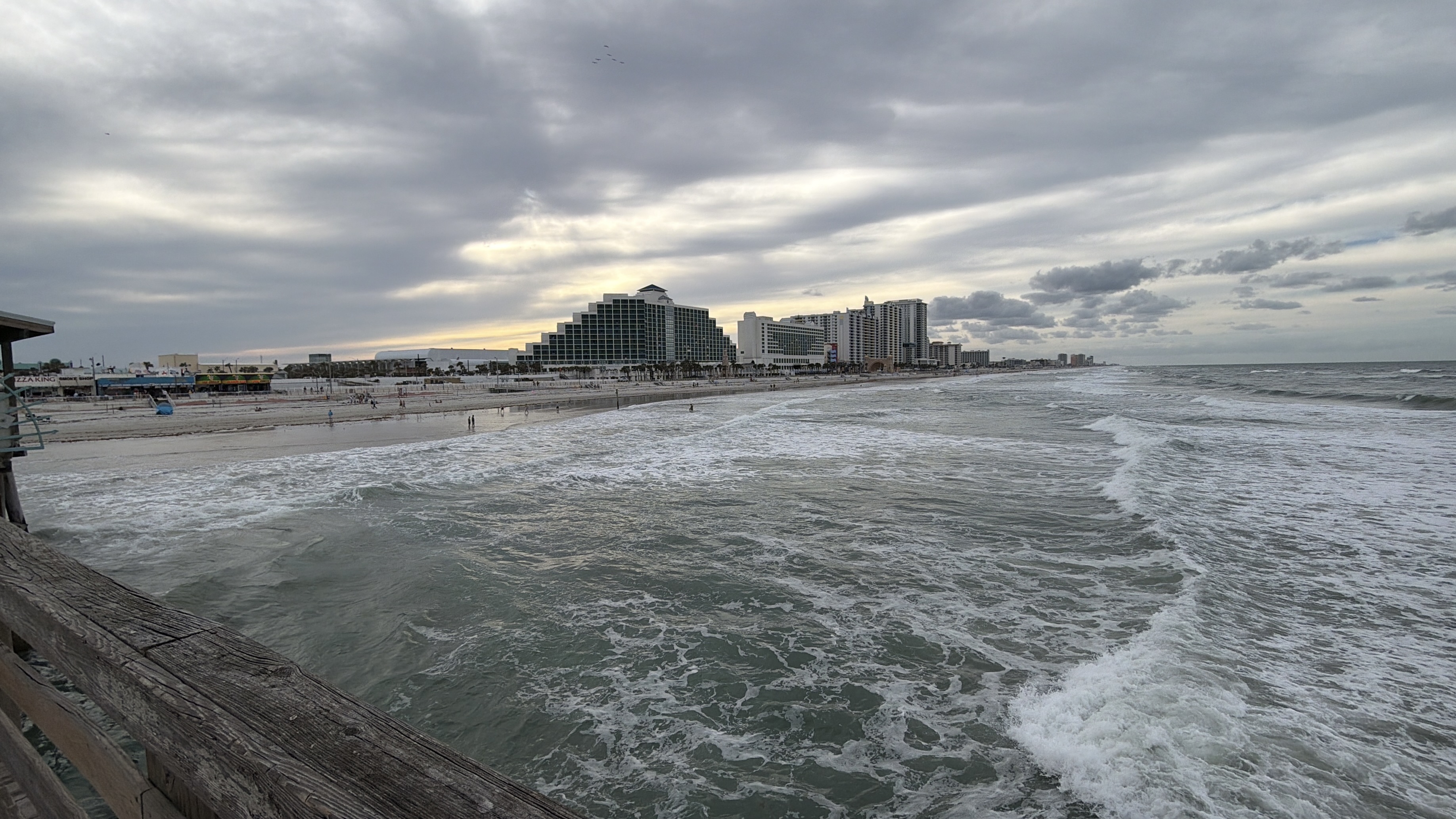 Daytona Beach ocean waves, pier railing, white sand, and beachfront hotels